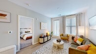 This single-floor residence at 9400 State Ave in Kansas City, Kansas, presents a thoughtfully designed layout with a contemporary aesthetic throughout. The living area serves as the heart of the unit, featuring light hardwood-style flooring, soft neutral wall tones, and large windows fitted with blinds and drape panels that allow generous natural light to fill the space. The open layout connects seamlessly to the bedroom, which is accessible through a clean white doorframe and offers plush carpeting, a dedicated window for additional natural light, and direct access to both a closet and the bathroom.

The kitchen is well-equipped with white shaker-style cabinetry, a classic subway tile backsplash, and stainless steel appliances including a range, microwave, and refrigerator. A spacious island with light countertops provides bar-style seating for multiple guests and pendant globe lighting overhead adds a refined touch. The galley-style workspace offers ample counter space on both sides for practical use.

The bathroom maintains the unit's clean, modern character with white cabinetry, a neutral countertop, an undermount sink, and a tiled tub-shower combination enclosed with a sliding glass door. Consistent finishes and a cohesive neutral palette create a polished, comfortable ambiance throughout the entire space.