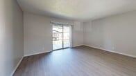 This thoughtfully updated unit at 8911 Northeastern Blvd NE in Albuquerque offers a clean, modern aesthetic across a comfortable single-floor layout. Light wood-tone vinyl flooring flows seamlessly throughout every room, complemented by neutral gray walls and textured ceilings that lend a cohesive, contemporary feel.

The kitchen is a standout feature, showcasing two-tone cabinetry with white upper cabinets and gray lower cabinets, crisp white quartz-style countertops, a classic subway tile backsplash, and stainless steel appliances including an electric range and dishwasher. A half-wall with pendant lighting connects the kitchen to the living area, creating an open, sociable layout. The living room is bright and airy, anchored by a sliding glass door that fills the space with natural light and provides access to an outdoor view.

The primary bedroom is generously proportioned, featuring a ceiling fan with light fixture and a window with blinds for natural light and privacy. The second bedroom is bright and well-sized, with its own closet and easy hallway access. The full bathroom is clean and functional, featuring a tiled shower-tub combination, a gray vanity with white countertop, and a frosted window for natural light. The hallway efficiently connects all rooms, completing this well-organized and move-in-ready home.