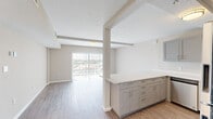 This single-floor, one-bedroom, one-bathroom unit offers a thoughtfully designed open-concept layout that maximizes its compact footprint. Light wood-look flooring runs continuously throughout the space, lending a cohesive and airy feel to every room.

The kitchen is well-appointed with gray shaker-style cabinetry, brushed nickel hardware, light quartz countertops, and a full suite of stainless steel appliances, including a refrigerator, range, microwave, and dishwasher. A peninsula counter extends into the living area, creating a natural visual division between the kitchen and living room while providing additional workspace and casual seating potential.

The living room benefits from an abundance of natural light delivered through a large sliding glass door fitted with vertical blinds, offering outdoor views and direct access to fresh air. Beamed ceiling details add architectural character to the shared living and kitchen space.

The bedroom is a comfortable, well-proportioned room featuring a window with outdoor views, a louvered bifold closet, and continued wood-look flooring. The bathroom is clean and functional, equipped with a full soaking tub and tub surround finished in large-format white tiles with chrome fixtures. The overall palette of warm neutral tones throughout creates a calm, move-in-ready ambiance.