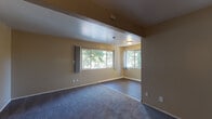 Located at 1767 Woodland Ave in East Palo Alto, California, this single-floor unit offers a practical and well-organized layout with distinct living, kitchen, bedroom, and bathroom areas. The living space is generously sized, featuring plush carpeting and multiple windows that frame views of mature surrounding trees, filling the room with natural light and a sense of connection to the outdoors. A structural beam detail separates portions of the living area, adding architectural character to the open floor plan. The galley-style kitchen is efficiently designed with warm honey-toned wood cabinetry lining both walls, dark granite-style countertops, a double sink, and white appliances including a range and refrigerator. Wood-look flooring runs throughout the kitchen, providing a clean contrast to the cabinetry. The bedroom is a comfortable, carpeted retreat with a closet and a large window offering views of the tree-lined street below. A full bathroom features a white tiled tub and shower combination, wood-look flooring, and warm neutral wall tones. Throughout the unit, the warm beige and tan color palette creates a cohesive and inviting ambiance, while the abundance of windows ensures bright, airy interiors across all rooms.