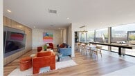 Located at 1775 N American St in Philadelphia's vibrant 19122 corridor, this thoughtfully designed single-floor community space offers a generous, open-plan layout that seamlessly integrates multiple social zones. Light-toned hardwood flooring flows throughout, unifying the space and complementing its contemporary aesthetic.

The living area is anchored by a full-wall wood-paneled entertainment unit housing a large flat-screen display, surrounded by bold terracotta velvet seating and colorful modern artwork that adds an energetic character to the room. Adjacent to this, a dedicated lounge zone features a full-sized pool table bathed in natural light pouring through dramatic floor-to-ceiling glass walls, which frame sweeping views of the surrounding Philadelphia streetscape and outdoor terrace.

The dining area is equally impressive, centered around a long communal table illuminated by a cascading cluster of brushed gold pendant lights. A built-in wet bar and beverage station anchored by a "Gather" sign serves the space, while a shuffleboard table offers additional entertainment. A separate, more intimate dining nook features a round stone-topped table and a richly stocked built-in bookshelf with live greenery. Large windows throughout ensure the entire space is filled with natural light, while glass doors provide seamless access to a spacious outdoor terrace with lounge seating.