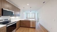 Located at 1455 Moonrise Avenue in Carrollton, TX, this well-designed one-bedroom, one-bathroom residence offers a thoughtfully organized single-floor layout. The open-concept kitchen and living area serves as the heart of the home, featuring rich wood-grain cabinetry, stainless steel appliances including a range, microwave, and dishwasher, and a sleek white countertop peninsula with an undermount sink. Pendant lighting adds a modern touch above the kitchen, while warm bamboo-style hardwood flooring flows consistently throughout the main living areas. The living room is bright and airy, benefiting from multiple windows dressed with horizontal blinds that invite natural light and outdoor views. A ceiling fan overhead enhances comfort throughout the space. The bedroom is a comfortable retreat with plush carpeting, additional windows for natural light, and its own ceiling fan. The full bathroom is well-appointed with dual vanity sinks, wood-tone cabinetry, a tiled soaking tub and shower combination, and continued hardwood flooring. A dedicated closet provides practical storage. Clean white walls and a neutral color palette throughout give the space a fresh, modern ambiance that is both functional and inviting.