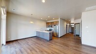 This single-floor residence is designed with a practical, open-concept layout that connects the kitchen and living area into one cohesive space. The kitchen serves as a central focal point, featuring a peninsula with a built-in sink and light countertops, warm wood-toned cabinetry, a tile backsplash, and a full suite of stainless steel appliances including a refrigerator, electric range, and microwave. Recessed lighting and a pendant fixture illuminate the space, while durable wood-look flooring extends throughout the main living area.

Two carpeted bedrooms offer a quieter, softer underfoot experience, each with windows fitted with blinds that allow for natural light and privacy. The bathrooms include a full bath with a tub-shower combo, wood-toned vanity, white countertop, and wood-look flooring, as well as a separate bathroom with a walk-in shower stall. A dedicated laundry room accommodates a full-size washer and dryer side by side, with wire shelving above for additional storage.

The attached two-car garage features a paneled door with transom windows and a concrete floor, providing generous vehicle and storage space. The overall design balances functionality with clean, contemporary finishes throughout.