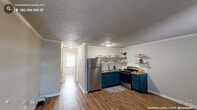 Located at 219 S East St in downtown Raleigh, NC, this one-bedroom unit offers a practical and well-appointed single-floor layout. Rich, dark hardwood-style flooring runs throughout, providing a warm and cohesive look across every room.

The living area greets you at entry through a modern front door with glass panel inserts, filling the space with natural light. Crown molding and a textured ceiling add classic character to the open room.

The kitchen is efficiently designed and features bold navy-blue lower cabinets topped with butcher block-style countertops, open wood shelving, stainless steel appliances including a refrigerator and range, and a functional sink — all contributing to a stylish yet practical cooking space.

A hallway connects the main living area to the bedroom, which is generously proportioned and bathed in natural light from a window with white blinds. The bedroom includes a dedicated closet and baseboard heating, offering year-round comfort. A wall-mounted PTAC unit provides additional climate control.

Neutral gray walls throughout create a calm, versatile backdrop, while the textured ceilings and crisp white trim lend the space a tidy, finished appearance. This unit is ideal for those seeking a straightforward, move-in-ready home in a central Raleigh location.