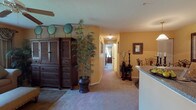 This single-floor residence offers a thoughtfully designed layout that balances comfort and functionality throughout. The living area serves as the heart of the home, featuring warm golden walls, plush carpeting, and a ceiling fan overhead. Large windows dressed with layered curtains and vertical blinds allow natural light to fill the room, while a hallway connects the main living spaces to the private quarters. A large armoire and decorative accents, including tall potted bamboo plants, add character to the space.

The kitchen is efficiently arranged with granite-style countertops, light wood cabinetry, a coil-burner range, refrigerator, and an overhead exhaust hood — providing all essential cooking amenities in a compact, functional footprint.

The primary bedroom is a serene retreat, highlighted by a substantial wooden headboard, coordinating nightstands, wall art, and a window dressed with elegant drapery. It is complemented by a generously sized walk-in closet with built-in wire shelving. A second bedroom features louvered closet doors, a ceiling fan, and ample room for furnishings.

Two bathrooms serve the residence: one with a tub-shower combination, tile surround, and granite-topped vanity, and a second with a similar refined aesthetic. Throughout, the warm tones, textured ceilings, and carpet flooring create a cohesive and inviting ambiance.