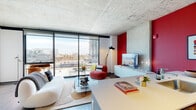 Located at 160 N Elizabeth Street in Chicago's vibrant West Loop neighborhood, this contemporary residence showcases an industrial-modern aesthetic defined by striking exposed concrete ceilings and expansive floor-to-ceiling windows that frame panoramic city views. The open-plan living and dining area is anchored by wide-plank hardwood-style flooring, with the seamless layout allowing natural light to pour through the oversized glazing throughout the day. A bold red accent wall energizes the living space, where the kitchen flows directly into the dining and lounge areas, offering a stainless steel appliance suite — including a gas range, built-in microwave, and full-size refrigerator — set against crisp white cabinetry and light wood flooring. The bedroom continues the floor-to-ceiling window theme, delivering unobstructed views of the Chicago skyline and surrounding cityscape, complemented by the same exposed concrete ceiling that ties the design together. The bathroom features a clean, contemporary finish with subway tile surrounding the shower/tub combination, a backlit vanity mirror, and a grey double-door vanity with ample storage. This residence presents a cohesive blend of raw industrial character and refined modern living in one of Chicago's most sought-after neighborhoods.