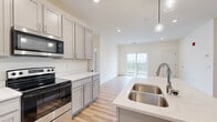 This well-appointed 2-bedroom, 2-bathroom unit in Enola, PA offers a thoughtfully designed single-floor layout with modern finishes throughout. The open-concept kitchen and living area serves as the heart of the home, showcasing gray shaker-style cabinetry, quartz countertops, stainless steel appliances including an electric range and built-in microwave, and a central island with a double undermount sink and pendant lighting. Light hardwood-style flooring runs throughout the main living areas, adding warmth and continuity. The living room is bright and airy, with recessed lighting and sliding glass doors that open onto a private balcony with outdoor views. Both bedrooms are carpeted and generously sized, each featuring a closet with wire shelving. The primary bedroom offers comfortable proportions with its own dedicated closet space. The two bathrooms are finished with gray vanity cabinetry, white quartz countertops, and hardwood-style flooring; one features a walk-in shower, while the other includes a vanity with overhead lighting. A dedicated closet area is conveniently located near the in-unit washer, adding practical storage solutions. The overall ambiance is clean, bright, and move-in ready, with a cohesive modern aesthetic throughout.