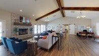 Located at 699 Wellingshire Blvd in Worthington, Ohio, this single-floor space offers a thoughtfully designed interior that blends rustic charm with modern sensibility. The main gathering area immediately draws attention with its soaring vaulted ceiling, adorned with rich, dark-stained exposed wood beams that add warmth and architectural character. A striking floor-to-ceiling stacked stone fireplace serves as a focal point along one wall, complemented by a mounted flat-screen television above it, making the space both functional and inviting.

Rich hardwood flooring runs throughout the open layout, anchoring a comfortable seating arrangement that includes upholstered sofas and accent chairs, ideal for relaxed gatherings or casual meetings. A long communal table with seating provides a collaborative workspace within the same open area. Natural light flows in generously through multiple sets of French doors and large windows, creating a bright and airy atmosphere.

A classic white barn door on a sliding track adds a stylish farmhouse touch and leads to an adjoining room, offering separation while maintaining the cohesive aesthetic. A decorative chandelier contributes an elegant finishing detail to the space. Overall, the design strikes a welcoming balance between cozy residential warmth and practical, community-oriented functionality.