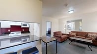 Located at 327 Eddy St in Ithaca, NY, this six-bedroom, two-bathroom unit is thoughtfully laid out across a single floor. The combined kitchen and living area serves as the heart of the unit, featuring dark granite-style countertops, white cabinetry, a coil-top electric range, and a built-in microwave set against a bold red accent wall. The living room offers carpeted flooring, two plush sofas, a wall-mounted flat-screen TV, and a central coffee table, creating a comfortable shared gathering space. A hallway connects the common areas to the private bedrooms and bathrooms. Each bedroom is equipped with carpeted flooring, a dresser, a desk with a chair, and individual climate control units. Several bedrooms benefit from large windows that invite natural light and provide views of surrounding greenery. The two full bathrooms are finished with light tile flooring, vanities with ample cabinet storage, large mirrors, and shower/tub combos with sliding glass doors — one bathroom features a double-sink vanity. The unit's straightforward layout and well-distributed room count make it well-suited for shared occupancy in the Ithaca area.