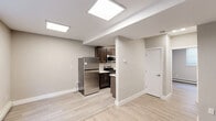 This efficiently designed 2-bedroom, 1-bathroom unit offers a well-organized single-floor layout with clean, modern finishes throughout. Light hardwood-style flooring runs continuously across all rooms, creating a cohesive and bright aesthetic. Flush panel ceiling lights illuminate the open living and kitchen areas, complementing the natural light admitted through blinded windows.

The kitchen is a functional standout, featuring dark espresso cabinetry, light countertops with a built-in sink, and a full suite of stainless steel appliances including a refrigerator, gas range, and over-the-range microwave. The kitchen flows openly into the main living area, making the space feel connected and practical.

The primary bedroom is a comfortable size, equipped with two side-by-side closets offering generous storage, a baseboard heating unit, and a window with blinds. The second bedroom is a cozy, well-lit room with a window and baseboard heat, suitable for a guest room or home office.

The bathroom is finished with elegance, showcasing marble-style tile wainscoting, a white vanity with an integrated sink, a wall-mounted mirror, and a clean, modern toilet — all contributing to a polished, spa-like atmosphere.

Throughout the unit, neutral warm-gray wall tones and crisp white trim create a calm, move-in-ready environment ideal for comfortable everyday living.