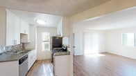 Located at 444 4th, Unit #324 in Escondido, this single-floor residence offers a well-designed layout with modern updates throughout. The galley-style kitchen is a standout feature, outfitted with crisp white shaker cabinetry, a decorative mosaic tile backsplash, dark countertops, a stainless steel double-basin sink, and black appliances including a coil-top range, refrigerator, and dishwasher. A window at the end of the kitchen brings in natural light and adds a sense of openness to the space. The kitchen connects seamlessly to the adjacent living and dining areas, where warm wood-look laminate flooring extends throughout. The living area is generously sized, featuring a textured ceiling, large windows with blinds, and sliding glass doors that allow abundant natural light to fill the room. The bedroom spaces are well-proportioned, each with matching wood-look flooring, neutral white walls, a textured ceiling, and windows that invite natural light. The bathroom includes a clean, white-tiled tub and shower combination with chrome fixtures. The overall aesthetic is bright, clean, and move-in ready, with consistent finishes creating a cohesive and functional living environment.