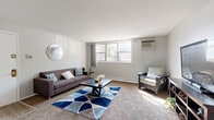 Located at 316 W 34th St in Steger, Illinois, this single-floor unit offers a straightforward and functional layout designed for comfortable everyday living. The generously sized living room serves as the heart of the space, featuring wall-to-wall carpeting, neutral white walls, and multiple windows that invite an abundance of natural light and offer views of the surrounding tree-lined exterior. A wall-mounted air conditioning unit and baseboard heating ensure year-round comfort throughout the living area. The bedroom continues the same carpeted flooring and neutral palette, with a window providing natural light and a peaceful atmosphere. A separate room with carpet and a paneled door offers additional flexible living space. The kitchen is equipped with warm oak cabinetry, white appliances including a gas range, dishwasher, and refrigerator, complemented by light countertops and wood-look flooring. A dedicated dining area adjacent to the kitchen provides space for meals. The bathroom features classic yellow ceramic tile accents, a wood-framed vanity with a mirrored medicine cabinet, a tub and shower combination, and wood-look flooring. Throughout the unit, the clean, light color scheme and practical finishes create a welcoming and easy-to-maintain living environment.