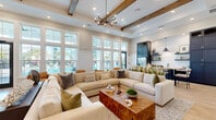 Located in Venice, Florida, this single-story community clubhouse offers a thoughtfully designed gathering space that blends coastal charm with modern sophistication. The welcoming entrance lobby features herringbone wood-panel accent walls, light hardwood flooring, bold navy cabinetry, and a striking pendant light, setting an inviting tone from the moment you step inside. A curated seating area with rounded lounge chairs provides a comfortable spot for casual conversations.

The expansive main lounge is anchored by soaring ceilings with exposed wood beams and shiplap detailing, a dramatic chandelier, and a wall of oversized windows that flood the space with natural light and frame views of the outdoor pool area. A generously sized sectional sofa surrounds a live-edge wood coffee table, creating an ideal setting for relaxation or socializing. A dedicated media nook showcases a bold, artistic tile feature wall in layered blue tones with navy built-in cabinetry below.

A secondary sitting area offers intimate seating around a round marble-top table, bathed in natural light from tall windows. The kitchenette is outfitted with quartz countertops, a stainless steel undermount sink, matte black fixtures, a white subway tile backsplash, and navy open shelving. A fully equipped fitness center with glass door access completes this well-appointed community facility.