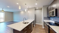 Located at 128 Florence St in Asheville, NC, this contemporary single-floor residence offers a thoughtfully designed open-concept layout with modern finishes throughout. The kitchen serves as the centerpiece of the living space, featuring a large island with a white quartz countertop, an undermount stainless steel sink, and elegant pendant lighting overhead. Dark espresso cabinetry provides ample storage, while a full suite of stainless steel appliances — including a refrigerator, range, microwave, and dishwasher — adds a sleek, functional touch. A blue subway tile backsplash introduces a pop of color and visual interest. Warm hardwood-style flooring flows through the main living areas, lending a cohesive and inviting feel. The living room is bright and open, with recessed lighting and direct access to a private balcony that offers pleasant outdoor views. The bedrooms are finished with plush carpeting, ceiling fans, and large windows that allow natural light to fill each room. A well-appointed bathroom features a tiled shower-tub combo with brushed nickel fixtures set against cool blue-gray walls. Throughout the unit, neutral tones, clean lines, and quality finishes create a modern and comfortable living environment well-suited for everyday life in the heart of Asheville.