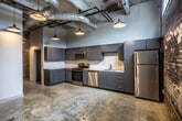 This single-floor loft in Memphis, Tennessee, showcases a compelling blend of industrial heritage and contemporary design. Exposed brick walls and polished concrete floors throughout establish a distinctive urban aesthetic, while exposed ductwork and pendant lighting add to the loft's raw, warehouse-inspired character.

The open kitchen is well-appointed with sleek gray cabinetry, stone-look countertops, a white subway tile backsplash, and a full suite of stainless steel appliances including a range, dishwasher, microwave, and refrigerator. The kitchen flows naturally into the main living area, where soaring ceilings and exposed overhead piping reinforce the industrial ambiance.

The bedroom offers a clean, neutral palette with polished concrete flooring and exposed ceiling elements, providing a versatile canvas for furnishing. A spacious walk-in closet with wire shelving offers generous storage capacity.

The bathroom is finished in crisp white, featuring a full-size soaking tub with shower combination, tile surround, and stone-look flooring, delivering a clean and functional space. Overall, this loft provides a well-balanced living environment that honors its building's historic character while incorporating modern conveniences throughout.