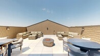 Located at 77 S Adams St in Oswego, Illinois, this single-level outdoor rooftop terrace offers a well-appointed open-air retreat designed for both relaxation and social gatherings. The space is finished with large-format, light-toned patio tiles that lend a clean, modern aesthetic throughout.

A central stone fire pit bowl serves as the focal point of the terrace, providing a natural gathering spot surrounded by ample open space. Multiple distinct seating zones are thoughtfully arranged across the terrace. One area features a generous wicker sectional sofa with neutral cushions paired with a wicker dining table and ottomans, creating a comfortable lounge setting. Additional dining areas include round tables with contemporary chairs, offering flexible options for casual meals or conversation.

The terrace is enclosed by textured masonry walls finished in a warm tan tone, which provide privacy while complementing the overall design. A set of glass-paneled double doors connects the outdoor space to an interior area, ensuring seamless indoor-outdoor flow. The open-sky orientation allows for abundant natural light throughout the day and clear views of the surrounding Oswego neighborhood and treetops beyond the perimeter walls.

This rooftop terrace is a versatile, well-designed outdoor space that balances comfort and functionality in a thoughtfully landscaped setting.