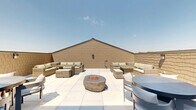 Located at 77 S Adams St in Oswego, Illinois, this single-level outdoor rooftop terrace offers a well-appointed open-air retreat designed for both relaxation and social gatherings. The space is finished with large-format, light-toned patio tiles that lend a clean, modern aesthetic throughout.

A central stone fire pit bowl serves as the focal point of the terrace, providing a natural gathering spot surrounded by ample open space. Multiple distinct seating zones are thoughtfully arranged across the terrace. One area features a generous wicker sectional sofa with neutral cushions paired with a wicker dining table and ottomans, creating a comfortable lounge setting. Additional dining areas include round tables with contemporary chairs, offering flexible options for casual meals or conversation.

The terrace is enclosed by textured masonry walls finished in a warm tan tone, which provide privacy while complementing the overall design. A set of glass-paneled double doors connects the outdoor space to an interior area, ensuring seamless indoor-outdoor flow. The open-sky orientation allows for abundant natural light throughout the day and clear views of the surrounding Oswego neighborhood and treetops beyond the perimeter walls.

This rooftop terrace is a versatile, well-designed outdoor space that balances comfort and functionality in a thoughtfully landscaped setting.