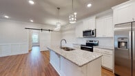 This single-story home blends modern farmhouse aesthetics with functional design throughout its thoughtfully laid-out floor plan. The kitchen serves as a central highlight, showcasing a large island with a granite countertop, an undermount double sink, and stylish pendant lighting overhead. White shaker cabinetry lines the walls, complemented by a subway tile backsplash and a full suite of stainless steel appliances, including a side-by-side refrigerator with ice and water dispenser, electric range, and over-the-range microwave. A distinctive sliding barn door provides a charming transition to an adjacent room, adding a farmhouse-inspired touch to the space.

Warm hardwood flooring flows consistently throughout the home, tying each room together cohesively. The bedrooms are bright and airy, featuring crown molding, ceiling fans with recessed lighting, and windows that invite natural light and outdoor views. One bedroom features a shiplap accent wall, adding additional character.

The bathrooms are finished with granite-topped white vanities, hardwood-style flooring, and a tub-shower combination with brushed nickel fixtures. A dedicated laundry room accommodates a full-size washer and dryer alongside overhead shelving for added storage. Crown molding and recessed lighting appear consistently throughout, contributing to a clean, polished ambiance.