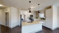 This single-floor home showcases a thoughtfully designed interior with a cohesive modern aesthetic. The kitchen serves as a central highlight, featuring white shaker-style cabinetry, light quartz countertops, and a sage green subway tile backsplash that adds a subtle pop of color. A generously sized center island with an undermount sink and matte black faucet provides additional workspace and is illuminated by two industrial-style pendant lights. Stainless steel appliances, including a French door refrigerator, electric range, and built-in microwave, complete the functional layout. Dark hardwood-style flooring runs through the kitchen and living areas, contrasting with the bright white walls and cabinetry.

The open living area is spacious and well-lit, equipped with a ceiling fan and flows seamlessly from the kitchen. Bedrooms feature plush carpeting, ceiling fans, and windows that bring in natural light. At least one bedroom includes access to a walk-in closet with built-in shelving. The bathrooms are finished with white shaker vanities, dark quartz countertops, matte black hardware, and large-format tile flooring. One bathroom includes a tiled walk-in shower with glass enclosure, adding a refined touch to the space.