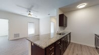 This well-designed single-floor unit offers a thoughtful open-concept layout that seamlessly connects the kitchen and living area. The kitchen is a standout feature, showcasing rich dark cabinetry with brushed nickel hardware, granite countertops, and a large peninsula island with an undermount sink — ideal for both meal preparation and casual dining. Stainless steel appliances, including a refrigerator, range, and microwave, complete the functional kitchen space. The open living area benefits from natural light streaming through blinds-covered windows and is finished with warm wood-look luxury vinyl plank flooring that extends throughout the unit. A ceiling fan in the living area adds comfort and airflow. The bedrooms are generously sized, each with ample closet space — one featuring a walk-in closet with built-in shelving. The bathrooms are well-appointed, with one featuring a granite-topped dark vanity, a large mirror, tile flooring, and open shelving for storage. The second bathroom includes a sleek glass-enclosed walk-in shower with white tile surround and brushed nickel fixtures. Throughout the unit, neutral walls and clean finishes create a bright, move-in-ready atmosphere suitable for a variety of lifestyles.