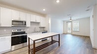 This well-appointed single-floor residence offers a thoughtfully designed open-concept layout that seamlessly connects the kitchen and living areas. The kitchen is a standout feature, showcasing crisp white shaker cabinetry, a classic subway tile backsplash, granite countertops, and a full suite of stainless steel appliances including a refrigerator, range, microwave, and dishwasher. A central kitchen island with a striking white marble-style top and dark wood base provides additional prep space and serves as a natural gathering point.

The living area flows naturally from the kitchen and features warm wood-style flooring and a ceiling fan, with a glass door opening to a private balcony that brings in abundant natural light. The bedrooms are carpeted for comfort, each equipped with ceiling fans and windows that allow for ample daylight and outdoor views.

The bathroom is elegantly finished with white cabinetry, granite countertops, a large framed mirror, and a soaking tub surrounded by marble-style tile. Wood-style flooring carries through the bathroom for a cohesive aesthetic. A dedicated in-unit laundry room with a full-size washer and dryer and overhead shelving adds significant practicality. Recessed lighting and a neutral color palette throughout lend the space a clean, modern ambiance.