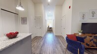 Located in Amherst, MA, this well-appointed single-floor unit offers a thoughtfully designed layout that balances functionality and modern style throughout. The open kitchen is a standout feature, showcasing gray shaker cabinetry, granite countertops, a herringbone tile backsplash, and a full suite of stainless steel appliances including a refrigerator, range, microwave, and dishwasher. A central island provides additional prep space and casual seating. Pendant lighting above the island adds a contemporary touch, and an in-unit stacked washer and dryer are conveniently located just steps away. The living area offers a comfortable gathering space with wood-look luxury vinyl plank flooring that runs throughout the unit, contributing to a clean, cohesive aesthetic. A long central hallway connects the various rooms, with recessed lighting overhead and crisp white walls lending a bright, airy feel. The bedrooms are cozy yet functional, each featuring a window that allows natural light and views of the surrounding greenery, along with space for a bed and a dedicated study desk area. The two full bathrooms are well-finished with granite-topped vanities, gray cabinetry, and tub-shower combinations, maintaining the same refined design palette found throughout the rest of the unit.