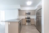 Located at 430 Ferndale Dr S in Barrie, Ontario, this well-designed one-bedroom, one-bathroom unit offers a thoughtfully efficient layout across a single floor. The open-concept kitchen and living area serves as the heart of the unit, featuring a large central island with a sleek quartz countertop, taupe cabinetry, and a full suite of stainless steel appliances including a refrigerator, electric range, built-in microwave, and dishwasher. Light wood-look flooring extends throughout the main living space, complementing the clean white walls and modern finishes. A sliding glass door in the living area opens to a private balcony, filling the space with natural light and offering views of the surrounding neighbourhood. The spacious primary bedroom includes a window with a neighbourhood view, a closet, and the same light flooring found throughout. The bathroom is finished with large-format tile flooring, a wide vanity with ample storage, and a tub-shower combination equipped with accessibility grab bars. A stacked in-unit washer and dryer adds everyday convenience. The overall aesthetic is clean, contemporary, and move-in ready.