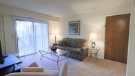 Located at 700 Roxalana Rd in Dunbar, West Virginia, this single-story space offers a cozy and well-maintained interior designed for comfortable everyday living. The living area serves as the focal point of the home, featuring plush wall-to-wall carpeting in a neutral tone that adds warmth underfoot and complements the light-colored walls throughout. A large sliding glass door fitted with vertical blinds allows an abundance of natural light to fill the room, creating a bright and airy atmosphere while providing access to the outdoors. The space accommodates a classic seating arrangement, with room for a sofa, accent chairs, and a glass-top coffee table, giving the area a functional yet refined feel. Framed artwork on the walls adds a touch of character, while table lamps provide soft, ambient lighting for evening hours. The overall design is understated and versatile, offering a clean canvas that adapts easily to various décor preferences. The single-floor layout ensures convenient accessibility throughout, making this a practical and inviting space suitable for a range of residents.