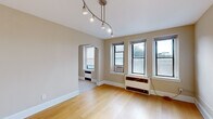 This 1-bedroom, 1-bathroom residence offers a comfortable and functional layout across a single floor. The living room is a bright, open space highlighted by warm hardwood flooring, neutral beige walls, and a sleek track lighting fixture overhead. A distinctive arched doorway connects the living area to the rest of the unit, adding a touch of classic architectural character. Multiple windows flood the space with natural light and provide outdoor views.

The kitchen features warm wood cabinetry, granite countertops, tile flooring, and black appliances, offering ample storage and counter space in a galley-style configuration. It is accessed via another elegant arched entryway.

The bedroom is a serene retreat with plush wall-to-wall carpeting, neutral tones, and two windows that allow for natural light and ventilation. A ceiling fan adds comfort, and a radiator unit ensures warmth during cooler months.

The bathroom is finished in crisp white, featuring classic black-and-white octagon tile flooring, subway tile walls, a full soaking tub with shower, a vanity with sink, and a window for natural ventilation.

Throughout the unit, clean white baseboards, consistent neutral color palettes, and thoughtful lighting create a cohesive, inviting ambiance.