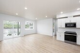 This single-floor unit offers a clean, contemporary design highlighted by light hardwood-style flooring and a neutral white-and-beige palette throughout. The open-concept living area flows seamlessly into the kitchen, creating a spacious and airy feel. Large sliding glass doors and multiple windows flood the main living space with natural light while providing views of the surrounding neighborhood.

The kitchen is well-appointed with white shaker-style cabinetry, light quartz countertops, a stainless steel undermount sink, and a full suite of stainless steel appliances including a gas range, built-in microwave, dishwasher, and a side-by-side refrigerator with ice and water dispenser. Recessed lighting adds a polished finish throughout.

The bedrooms are generously sized, each featuring the same warm hardwood-style flooring, recessed lighting, and windows that bring in natural light and outdoor views. A dedicated in-unit laundry area houses a full-size front-loading washer and dryer. The bathroom features light vinyl flooring and clean, minimal fixtures consistent with the modern aesthetic. The space as a whole presents a fresh, move-in-ready environment with thoughtful design and functional amenities throughout.