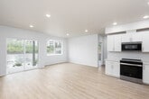 This single-floor unit offers a clean, contemporary design highlighted by light hardwood-style flooring and a neutral white-and-beige palette throughout. The open-concept living area flows seamlessly into the kitchen, creating a spacious and airy feel. Large sliding glass doors and multiple windows flood the main living space with natural light while providing views of the surrounding neighborhood.

The kitchen is well-appointed with white shaker-style cabinetry, light quartz countertops, a stainless steel undermount sink, and a full suite of stainless steel appliances including a gas range, built-in microwave, dishwasher, and a side-by-side refrigerator with ice and water dispenser. Recessed lighting adds a polished finish throughout.

The bedrooms are generously sized, each featuring the same warm hardwood-style flooring, recessed lighting, and windows that bring in natural light and outdoor views. A dedicated in-unit laundry area houses a full-size front-loading washer and dryer. The bathroom features light vinyl flooring and clean, minimal fixtures consistent with the modern aesthetic. The space as a whole presents a fresh, move-in-ready environment with thoughtful design and functional amenities throughout.