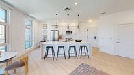 Located at 20 Medford St in Somerville, MA, this thoughtfully designed one-bedroom, one-bathroom residence offers a sleek, modern aesthetic throughout its well-appointed single floor. Light hardwood flooring flows continuously across the open-concept living area, creating a seamless and airy feel.

The kitchen serves as a central focal point, featuring a large waterfall-edge island with seating for four, crisp white cabinetry, stainless steel appliances, and pendant lighting overhead. A floor-to-ceiling window floods the space with natural light and frames views of the surrounding neighborhood. The open layout connects effortlessly to the dining and living areas, making the space ideal for entertaining.

The spacious bedroom is highlighted by a dramatic wall of oversized windows offering sweeping views of Somerville's streetscape and the surrounding brick architecture. A built-in double sliding closet provides generous storage, while the clean white walls and light flooring reinforce the home's contemporary character.

The bathroom is finished in a crisp, minimalist style with white tile, a soaking tub and shower combo, matte black fixtures, and a warm wood-toned vanity with an undermount sink and a large mirror.

Recessed lighting throughout and an abundance of natural light give this residence a bright, welcoming ambiance from every angle.