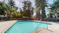 Located in Citrus Heights, California, this outdoor community amenity space centers around a generously sized swimming pool that serves as the focal point of the area. The pool is framed by a wide, open concrete deck offering ample room for lounge seating and sunbathing, making it well-suited for relaxation and recreation. A gated enclosure surrounds the pool area, providing both security and a sense of privacy for residents.

Adjacent to the pool, a secondary courtyard area features thoughtfully arranged landscaping, including decorative shrubs, ground cover plantings, and a central planter that add visual interest and a welcoming atmosphere. Tall, mature trees — including towering conifers and stately palm trees — provide natural shade and greenery, softening the hardscape and enhancing the outdoor ambiance.

The surrounding buildings reflect a classic California residential architectural style, with neutral stucco exteriors and low-pitched rooflines typical of the region. The single-story clubhouse or utility building adjacent to the pool area includes gated access points and informational signage, contributing to the functional layout of the community space. Under the abundant California sunshine, the entire outdoor area benefits from excellent natural light, creating a bright and inviting environment year-round.
