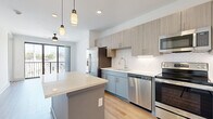 Located at 1001 16th Ave S in Nashville's vibrant 12 South neighborhood, this one-bedroom, one-bathroom unit offers a thoughtfully designed layout across a single floor. Light wood-tone flooring runs continuously throughout, creating a cohesive and clean aesthetic.

The kitchen is a standout feature, outfitted with two-tone cabinetry—soft blue lower cabinets paired with light wood upper cabinets—and a white herringbone tile backsplash. A quartz-topped island with built-in shelving provides additional prep and storage space, while pendant lighting overhead adds a modern touch. Stainless steel appliances include a refrigerator, range, microwave, and dishwasher.

The living area flows naturally from the kitchen and opens to a private balcony through floor-to-ceiling sliding glass doors, allowing abundant natural light and urban views. A ceiling fan enhances comfort in this space.

The bedroom is well-proportioned and includes a window with blinds, a ceiling fan, and access to a closet. The bathroom features a full soaking tub with marble-style surround, a gray vanity with quartz countertop, and wood-look flooring. A hallway connects the primary spaces efficiently, completing this well-appointed urban residence.