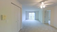 This single-floor residential space offers a clean, open layout designed to maximize comfort and functionality. The main living area is finished with plush wall-to-wall carpeting that adds warmth underfoot, while crisp white walls and ceilings create a bright, airy atmosphere throughout. A ceiling fan with an integrated light fixture is centrally positioned, providing both practical ventilation and ambient lighting to the space.

Natural light flows generously into the room through a large sliding glass door, which opens onto a balcony overlooking the surrounding residential neighborhood — a standout feature that enhances the sense of openness and connection to the outdoors. The sliding door serves as both a functional entry point to the exterior and a visual anchor that draws the eye across the room.

A set of built-in bifold closet doors along one wall offers convenient, organized storage without disrupting the clean lines of the interior. The overall design is neutral and understated, with a straightforward layout that lends itself well to a variety of furniture arrangements. The combination of natural light, soft carpeting, and a seamless indoor-outdoor connection gives the space a welcoming, livable quality that is both practical and comfortable.