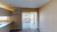 This single-floor unit offers a straightforward and functional layout designed for comfortable everyday living. The living area is generously proportioned, finished with neutral-toned carpet and warm beige walls under a textured ceiling, creating a simple and cohesive atmosphere. A wall-mounted air conditioning unit provides climate control, while a sliding glass door fitted with vertical blinds opens to a balcony, allowing natural light to filter into the space and offering an outdoor connection.

The kitchen is efficiently arranged, featuring built-in upper cabinetry with a wood-panel finish, a double-basin sink, a range, and a refrigerator. A pass-through countertop extends into the living area, adding functional workspace and an open feel between the two areas.

The bedroom is a well-sized, carpeted room with warm wall tones, a textured ceiling, and a window fitted with horizontal blinds that brings in natural daylight. Multiple electrical outlets and clean white baseboards complete the room.

The bathroom is neatly appointed with a single-sink vanity topped with a warm-toned countertop, white cabinetry with hardware, a mirrored medicine cabinet with overhead lighting, a toilet, and a shower/tub combination. Wood-look flooring adds warmth to the space. Overall, the unit presents a clean, functional environment suited for a variety of living arrangements.