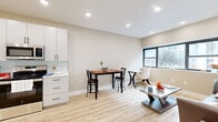 Located at 90 N Swan St in Albany, NY, this well-designed one-bedroom, one-bathroom unit offers a thoughtfully organized layout across a single floor. Light wood-tone flooring flows seamlessly throughout, creating a warm, cohesive aesthetic.

The kitchen is a standout feature, outfitted with crisp white cabinetry, black hardware accents, quartz countertops, a subtle tile backsplash, and a full suite of stainless steel appliances including a range, over-the-range microwave, dishwasher, and refrigerator. In-unit laundry is also present.

The combined kitchen and living area provides an open, functional layout. The living space benefits from natural light through large black-framed windows that offer views of the surrounding streetscape, and is climate-controlled via a wall-mounted mini-split unit.

The bedroom is a comfortable, quiet retreat featuring a window with urban views, a double closet with white paneled doors, and recessed lighting overhead.

The bathroom is elegantly appointed with large-format stone-look tile flooring, marble-style wall tile, a wood-toned vanity with gold hardware, a medicine cabinet with lighted mirror, and a shower-tub combination.