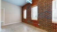 This thoughtfully designed one-bedroom, one-bathroom unit blends industrial character with modern finishes across a single floor of well-utilized living space. Exposed red brick walls serve as a defining architectural element throughout, lending an authentic, loft-inspired aesthetic that contrasts beautifully with the clean white trim and neutral paint tones. Polished concrete floors run seamlessly through every room, adding a sleek, durable foundation that enhances the urban feel.

The kitchen is well-appointed with crisp white shaker cabinetry extending to the ceiling for ample storage, white subway tile backsplash, light countertops, and a full suite of stainless steel appliances including a range, microwave, dishwasher, and refrigerator. Black hardware accents provide a contemporary finishing touch.

The main living area features large windows set into the brick wall, inviting generous natural light and views of the surrounding neighborhood. Exposed ductwork adds to the industrial charm of the space.

The bedroom is a comfortable size with its own walk-in closet equipped with multi-tier shelving and hanging rods. The bathroom offers a glass-enclosed walk-in shower with white tile surround, black fixtures, a white vanity, and built-in open shelving for added storage convenience.