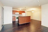 This single-floor residence offers a practical and comfortable layout designed for everyday living. The open-concept living and dining area is finished with rich, dark hardwood-style flooring and features a ceiling fan with light fixture overhead. A sliding glass door floods the space with natural light and opens to a private balcony with outdoor views, making it a standout feature of the living area.

The kitchen is positioned adjacent to the living space and includes warm-toned wooden cabinetry extending to the upper walls, laminate countertops, and white appliances including an electric range, over-the-range microwave, and refrigerator. A kitchen island with pendant lighting adds both workspace and visual separation from the main living area. A dedicated closet provides additional pantry or storage space nearby. In-unit side-by-side laundry is also conveniently located within the unit.

The two bedrooms are carpeted for comfort, each offering a closet and access to natural light through window blinds. Both bathrooms are equipped with wooden vanities, granite-style countertops, a toilet, and a full tub-shower combination. The dark hardwood-style flooring continues through the bathrooms, tying the space together cohesively throughout.