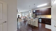 Located at 5400 Coraci Blvd in Port Orange, Florida, this 2-bedroom, 2-bathroom residence offers a thoughtfully designed open-concept layout across a single floor. The combined kitchen and living area serves as the heart of the home, where rich dark wood cabinetry, granite countertops, a decorative tile backsplash, and stainless steel appliances define a well-equipped kitchen. A central island with bar seating provides additional prep space and casual dining. Pendant lighting illuminates the island, while hardwood-style flooring flows seamlessly through the main living areas, adding warmth and continuity. The living room is bright and inviting, featuring large windows with blinds and sheer drapery that allow abundant natural light, along with direct access to an outdoor area. The spacious primary bedroom features plush carpeting and ample closet space, including a walk-in closet outfitted with wire shelving systems for organized storage. The second bedroom is equally comfortable, also carpeted and naturally lit. Both bathrooms are finished with granite-topped dark wood vanities and tile flooring, with one featuring a full soaking tub and shower combination. The overall ambiance is modern and cohesive, with neutral tones and quality finishes throughout.