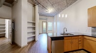 Located at 1550 Raleigh St in Denver's vibrant West Colfax neighborhood, this urban loft blends industrial character with modern finishes throughout its single-floor layout. Soaring exposed concrete ceilings with visible ductwork and steel conduit establish a distinctive loft aesthetic, while wide-plank hardwood-style flooring grounds the open living areas with warmth.

The kitchen is a standout feature, centered around a large island with a dark stone countertop, undermount sink, and pendant lighting overhead. Warm wood cabinetry lines the walls alongside a mosaic tile backsplash, and the space is fully equipped with stainless steel appliances including a refrigerator, range, and microwave. Built-in open shelving near the entry provides additional storage and display space.

The bedroom offers plush carpeting underfoot and continues the industrial ceiling aesthetic, with a stylish sliding barn door serving as a functional architectural accent. A generously sized walk-in closet features wire shelving and built-in shelves for ample organization. The bathroom is clean and well-appointed, with a full tub and shower, white tile surround, wood vanity with dark countertop, and open shelving. A dedicated in-unit laundry area adds everyday convenience to this well-designed urban retreat.