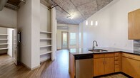 Located at 1550 Raleigh St in Denver's vibrant West Colfax neighborhood, this urban loft blends industrial character with modern finishes throughout its single-floor layout. Soaring exposed concrete ceilings with visible ductwork and steel conduit establish a distinctive loft aesthetic, while wide-plank hardwood-style flooring grounds the open living areas with warmth.

The kitchen is a standout feature, centered around a large island with a dark stone countertop, undermount sink, and pendant lighting overhead. Warm wood cabinetry lines the walls alongside a mosaic tile backsplash, and the space is fully equipped with stainless steel appliances including a refrigerator, range, and microwave. Built-in open shelving near the entry provides additional storage and display space.

The bedroom offers plush carpeting underfoot and continues the industrial ceiling aesthetic, with a stylish sliding barn door serving as a functional architectural accent. A generously sized walk-in closet features wire shelving and built-in shelves for ample organization. The bathroom is clean and well-appointed, with a full tub and shower, white tile surround, wood vanity with dark countertop, and open shelving. A dedicated in-unit laundry area adds everyday convenience to this well-designed urban retreat.