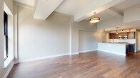 Located at 90 State St in the heart of Albany, NY, this thoughtfully designed unit offers a well-appointed single-floor layout. The open-concept living and kitchen area is anchored by rich hardwood flooring that flows throughout the space, complemented by neutral-toned walls and clean white baseboards that create a bright, airy atmosphere. Architectural beam detailing along the ceiling adds character, while stylish drum pendant lighting provides warm, functional illumination.

The kitchen is a standout feature, showcasing dark espresso shaker cabinetry, crisp white quartz countertops, and a classic white subway tile backsplash. Premium stainless steel appliances — including a professional-grade gas range, built-in microwave, and French door refrigerator — make this kitchen as functional as it is visually striking. Track lighting overhead ensures excellent task visibility.

The living area benefits from arched black-framed windows that invite natural light and offer views of the surrounding Albany cityscape. Elevated ceiling heights with exposed beam accents contribute to an open, loft-like feel.

The bathroom is finished with large-format gray marble-look tile flooring, a glass-enclosed walk-in shower with white subway tile surround, dark wood vanity cabinetry with a stone countertop, and brushed nickel hardware and grab bars throughout.