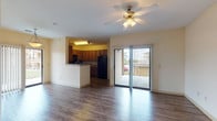 Located at 7601 Gateway Blvd in Live Oak, Texas, this single-floor residence offers a thoughtfully designed layout that balances open living spaces with private retreats. The main living area is anchored by durable wood-style flooring, a ceiling fan with light fixture, and a sliding glass door that fills the room with natural light and provides direct access to a generously sized covered balcony — ideal for outdoor relaxation. An elegant arched entryway connects the living area to the rest of the unit, adding architectural character to the interior. The kitchen is open to the living space via a raised breakfast bar and features rich wood cabinetry, dark granite-style countertops, a black tile backsplash, and a full suite of black appliances including a range, microwave, and refrigerator, all set on light wood-style flooring. The bedroom is carpeted for comfort and includes a ceiling fan, a window with outdoor views, and access to a spacious walk-in closet with wire shelving on multiple walls. The bathroom offers a granite-style vanity countertop with an integrated sink and large mirror. Wood-style flooring continues through the hallway, tying the private areas of the unit together cohesively.