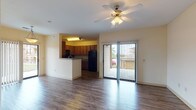 Located at 7601 Gateway Blvd in Live Oak, Texas, this single-floor residence offers a thoughtfully designed layout that balances open living spaces with private retreats. The main living area is anchored by durable wood-style flooring, a ceiling fan with light fixture, and a sliding glass door that fills the room with natural light and provides direct access to a generously sized covered balcony — ideal for outdoor relaxation. An elegant arched entryway connects the living area to the rest of the unit, adding architectural character to the interior. The kitchen is open to the living space via a raised breakfast bar and features rich wood cabinetry, dark granite-style countertops, a black tile backsplash, and a full suite of black appliances including a range, microwave, and refrigerator, all set on light wood-style flooring. The bedroom is carpeted for comfort and includes a ceiling fan, a window with outdoor views, and access to a spacious walk-in closet with wire shelving on multiple walls. The bathroom offers a granite-style vanity countertop with an integrated sink and large mirror. Wood-style flooring continues through the hallway, tying the private areas of the unit together cohesively.