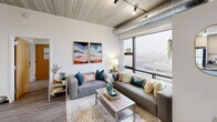 Located at 401 Thompson St in Ann Arbor, MI, this 2-bedroom, 2-bathroom unit delivers a distinct industrial-modern aesthetic across a single thoughtfully organized floor. The exposed concrete ceiling is a defining architectural feature throughout, complemented by track lighting and visible ductwork that reinforce the loft-inspired character of the space.

The open-plan living, dining, and kitchen area forms the heart of the unit. Large floor-to-ceiling windows flood the living room with natural light and frame elevated views of the surrounding Ann Arbor cityscape. The kitchen features an island with dark granite countertops, warm wood cabinetry, stainless steel appliances, and a stacked washer and dryer tucked neatly into a dedicated alcove. Open shelving adds both storage and visual interest.

Both bedrooms continue the exposed concrete ceiling aesthetic and feature hardwood-style flooring. The primary bedroom includes a window with urban views, while each bedroom offers access to a closet. Both bathrooms are finished with floating dark wood vanities, large mirrors, and clean white walls, with one bathroom featuring a tub-shower combination.

Hardwood-style flooring runs throughout the entire unit, tying the industrial and contemporary design elements together cohesively.