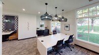 This single-floor office space is thoughtfully designed to blend functionality with contemporary style. The reception area welcomes visitors with large-format tile flooring, a tufted cognac leather banquette, and a beverage station set against a striking geometric patterned accent wall in charcoal and white, flanked by gray cabinetry — a polished and inviting first impression.

The collaborative work area features a generous white conference table surrounded by ergonomic mesh chairs, illuminated by a trio of dramatic wire-cage pendant lights. Natural light pours in through large windows that frame lush green outdoor views, creating a bright and energizing atmosphere. Framed artwork and a dark credenza add warmth and character to the space.

A cozy lounge nook is furnished with rich cognac leather armchairs and a round marble-top accent table, set beneath a large wall clock — ideal for relaxed conversations or casual waiting. Patterned carpeting flows throughout, tying the areas together with texture and visual interest.

Private consultation or interview rooms are accessible via sleek sliding doors, featuring bold geometric wallcovering in navy and white, built-in surfaces, and recessed lighting, offering a discreet and professional environment. Throughout the space, clean white walls, recessed lighting, and carefully curated décor create a cohesive, modern, and welcoming professional atmosphere.