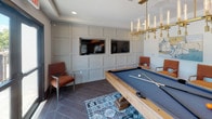 Located at 6352 W Longboat Blvd in Tampa, Florida, this single-floor clubhouse is a thoughtfully designed amenity space that blends upscale finishes with a welcoming, social atmosphere. The open layout is anchored by wood-look tile flooring laid in a sophisticated herringbone pattern, creating a cohesive flow throughout the space.

The centerpiece of the clubhouse is a stunning kitchen and bar area, featuring a large waterfall-edge quartz island with seating for multiple guests. Striking glass pendant lights with brass accents hang above, casting warm light over the space. Rich, dark wood cabinetry lines the walls, complemented by an intricate mosaic tile backsplash and a mirrored cabinet display that adds depth and elegance. A sink and prep area make the space fully functional for entertaining.

Adjacent to the kitchen is a comfortable lounge area furnished with a charcoal sofa accented by warm amber and patterned throw pillows. A large sliding glass door frames views of the outdoor pool and surrounding palm trees, filling the space with natural light. Bold, oversized wall art adds an artistic focal point to the room.

The game room offers a full-size billiards table set beneath a sleek brass candelabra-style chandelier. A wainscoted accent wall in soft gray hosts dual built-in flat-screen TVs, flanked by comfortable lounge chairs — ideal for socializing and recreation.