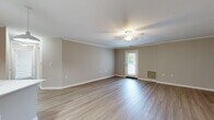 Located at Somerhill Farms in Gainesville, Virginia, this single-story residence showcases a clean, contemporary design with neutral warm-gray tones and consistent finishes throughout. The open-concept living area is a standout feature, offering generous square footage with smooth-finish ceilings accented by crown molding, a ceiling fan with integrated lighting, and luxury vinyl plank flooring that extends throughout the main living spaces. Natural light filters in through a glass-paneled exterior door, creating a bright and welcoming atmosphere.

The kitchen is well-appointed with white shaker-style cabinetry, light quartz countertops, a subway tile backsplash, and stainless steel appliances, including a refrigerator, electric range, microwave, and dishwasher. A central island with an undermount sink serves as a focal point, illuminated by two modern pendant lights. Crown molding carries through into the kitchen, reinforcing the cohesive design.

The bedroom features soft carpet flooring and a wide window with views of the surrounding greenery. Bathrooms are finished with white cabinetry, quartz countertops, brushed nickel fixtures, and wood-look flooring. One bathroom includes a glass-enclosed walk-in shower, while the other offers a tub-shower combination. A dedicated laundry area with overhead wire shelving accommodates a full-size washer and dryer.