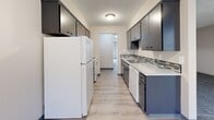 Located in Salem, Oregon, this two-bedroom, one-bathroom unit offers a well-organized single-floor layout designed for comfortable, everyday living. The combined kitchen and dining area serves as the heart of the home, featuring a galley-style kitchen with dark gray cabinetry, light stone-look countertops, a mosaic tile backsplash, and white appliances including a refrigerator and dishwasher. Light wood-style flooring runs through the kitchen and dining area, while a window at the end of the space brings in natural light. The adjacent living room provides an open, versatile space for relaxation and entertaining. Both bedrooms are carpeted in soft gray tones, offering a comfortable and quiet retreat. The spacious primary bedroom includes a built-in closet with shelving, while the second bedroom features a window with outdoor views and its own closet. A hallway connects the main living areas to the bedrooms, with additional closet storage available. The full bathroom is finished with wood-style flooring, a tub-shower combination, a vanity with stone-look countertop, and built-in cabinetry for storage. Textured ceilings are present throughout. This unit delivers a clean, practical layout suited for a range of residents in a residential Salem community.